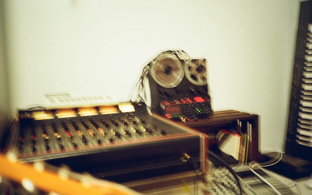 A vintage mixing console and reel-to-reel tape machine set up together in the room.